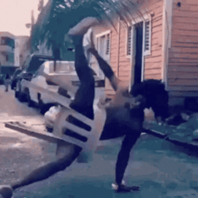 A Man Is Doing A Handstand With A Chair Around His Neck . GIF