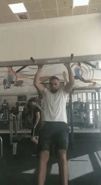A Man Is Doing A Pull Up Exercise In A Gym . GIF
