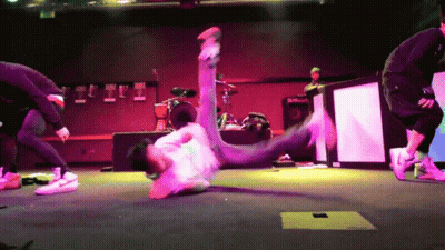 A Man Is Doing A Trick On A Stage With A Drum Set In The Background GIF