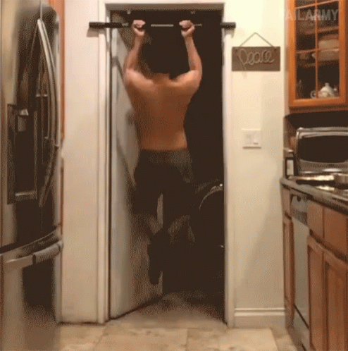 A Man Is Doing Pull Ups In A Kitchen With A Peace Sign Hanging On The Door GIF