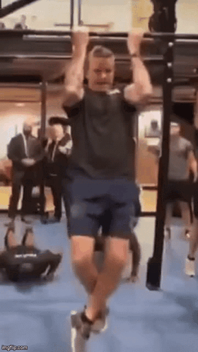 A Man Is Doing Pull Ups On A Bar In A Gym While People Watch . GIF