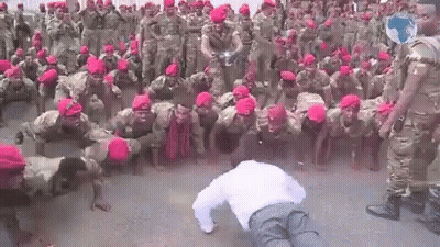 A Man Is Doing Push Ups In Front Of A Large Group Of Soldiers Wearing Red Hats . GIF