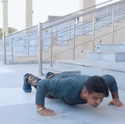 A Man Is Doing Push Ups On A Sidewalk In Front Of Some Stairs GIF