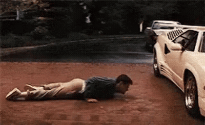 A Man Is Doing Push Ups On The Ground In Front Of A White Car GIF
