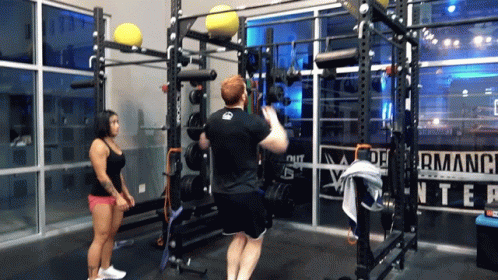 A Man Is Doing Squats In A Gym With A Woman Watching GIF