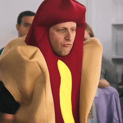 A Man Is Dressed As A Hot Dog With A Yellow Stripe GIF