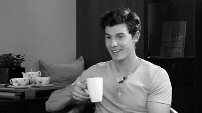 A Man Is Drinking A Cup Of Coffee While Sitting In A Chair . GIF