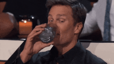 A Man Is Drinking A Glass Of Water With His Mouth Open . GIF
