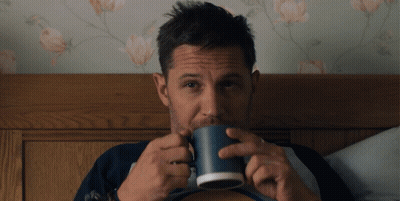 A Man Is Drinking From A Blue Mug In Bed GIF