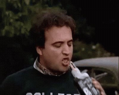 A Man Is Drinking From A Bottle While Wearing A College Sweater . GIF