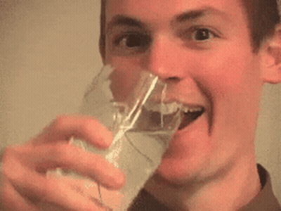A Man Is Drinking From A Glass And Smiling With His Tongue Out . GIF