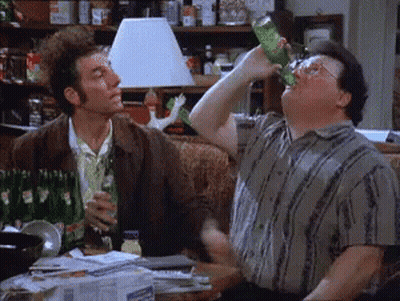 A Man Is Drinking From A Green Bottle While Another Man Looks On . GIF