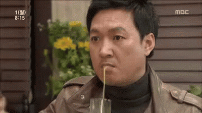 A Man Is Drinking Something Through A Straw From A Glass While Sitting At A Table . GIF
