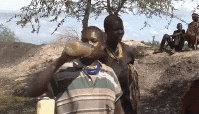 A Man Is Drinking Water From A Bottle While Another Man Sits On A Rock . GIF