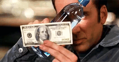 A Man Is Drinking Water From A Bottle While Holding A Dollar Bill . GIF
