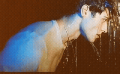 A Man Is Drinking Water From A Fountain With A Blue Light Behind Him GIF
