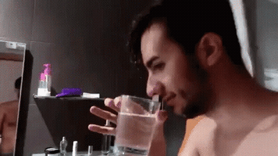 A Man Is Drinking Water From A Glass In A Bathroom . GIF