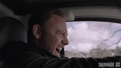 A Man Is Driving A Car And Laughing While Looking Out The Window . GIF