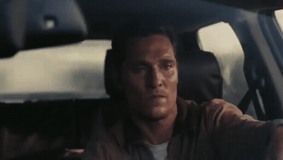A Man Is Driving A Car And Looking At The Camera . GIF