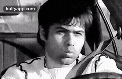 A Man Is Driving A Car And Making A Funny Face In A Black And White Photo . GIF