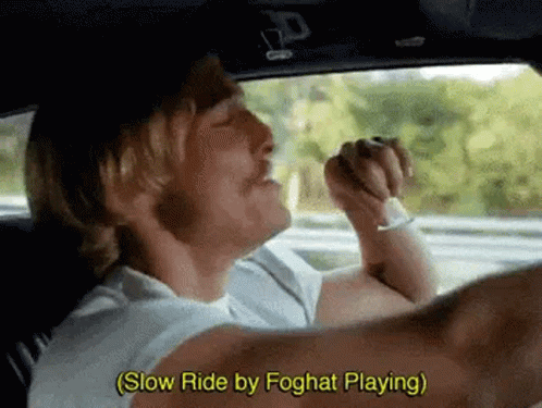 A Man Is Driving A Car And Singing While Holding A Cigarette In His Mouth . GIF