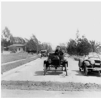 A Man Is Driving A Car Down A Street Next To A Convertible Car . GIF