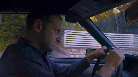 A Man Is Driving A Car With A Sticker On The Rear View Mirror That Says ' Volvo ' GIF