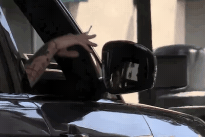 A Man Is Driving A Car With His Hands Out The Window . GIF