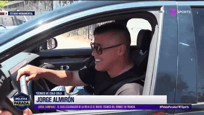 A Man Is Driving A Car With Jorge Almiron On The Screen GIF