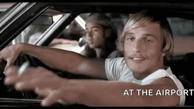 A Man Is Driving A Car With The Words `` At The Airport '' Written Above Him . GIF