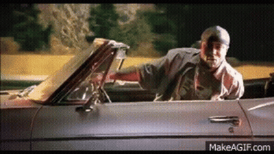 A Man Is Driving A Convertible Car On A Road . GIF