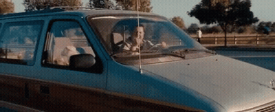 A Man Is Driving A Minivan Down A Road While Talking On A Cell Phone . GIF