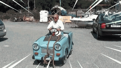 A Man Is Driving A Small Blue Car With A Rope Attached To The Front Of The Car GIF