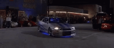 A Man Is Driving A Sports Car At Night In A Garage . GIF