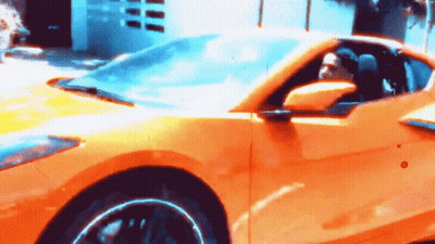 A Man Is Driving A Yellow Sports Car With A Blue Sky In The Background GIF