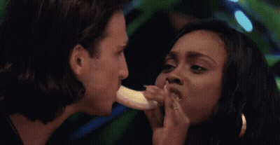 A Man Is Eating A Banana While A Woman Holds A Banana To His Mouth GIF