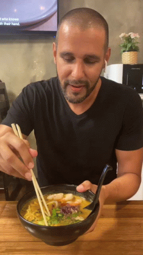 A Man Is Eating A Bowl Of Soup With Chopsticks GIF