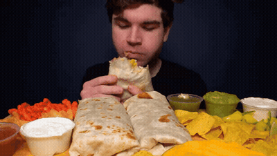 A Man Is Eating A Burrito Surrounded By Nachos And Sauces GIF