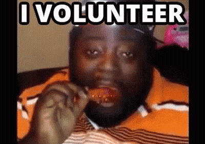 A Man Is Eating A Chicken Wing With The Words I Volunteer Behind Him GIF