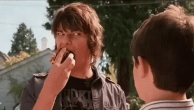 A Man Is Eating A Donut While Another Man Watches . GIF