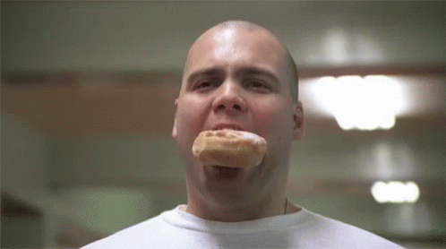 A Man Is Eating A Donut With His Mouth Open In A Room . GIF