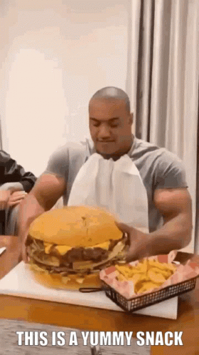A Man Is Eating A Giant Hamburger And French Fries . GIF