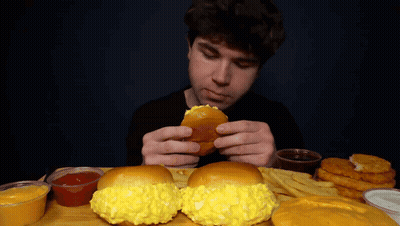 A Man Is Eating A Hamburger And French Fries At A Table GIF
