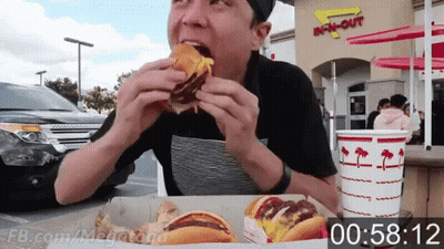 A Man Is Eating A Hamburger In Front Of An In N Out Restaurant GIF
