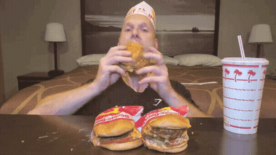 A Man Is Eating A Hamburger Next To A Bag Of Burger King GIF