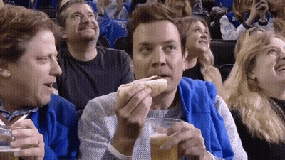 A Man Is Eating A Hot Dog And Drinking Beer While Watching A Game GIF