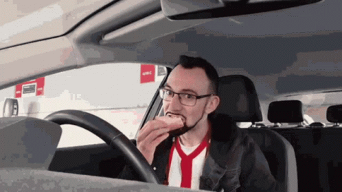 A Man Is Eating A Hot Dog While Driving GIF