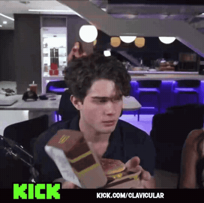 A Man Is Eating A Mcdonald 'S Hamburger In A Restaurant With Kick.com/clavicular On The Bottom GIF