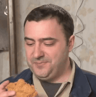 A Man Is Eating A Piece Of Fried Chicken While Looking At The Camera . GIF