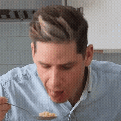 A Man Is Eating Food From A Spoon In A Kitchen . GIF